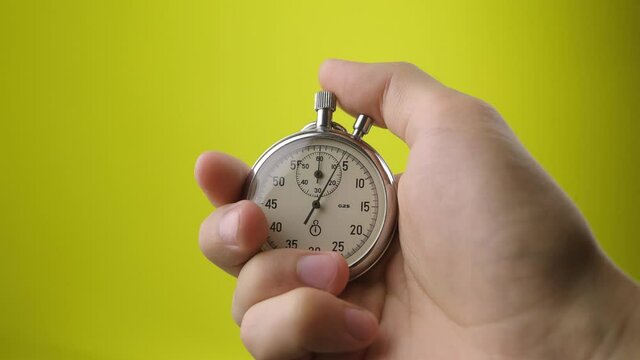 Male hand holding analogue stopwatch on yellow background. Time start with old chronometer man presses start button in the sport concept. Time management concept.