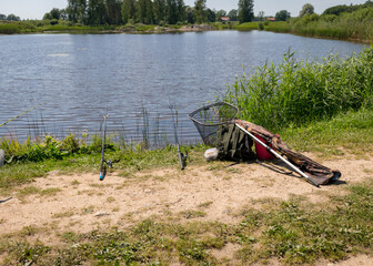Obraz na płótnie Canvas summer landscape by the lake, fishing tackle in the foreground, calm lake water, beautiful reflections in the water, summer