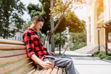 Happy young man freelancer is working outdoors on his computer laptop