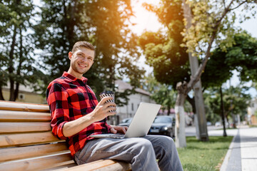 Fototapeta premium Happy young man freelancer is working outdoors on his computer laptop
