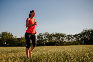 Young beautiful woman is making sport, she is running on a grass in the midst of nature on sunset.