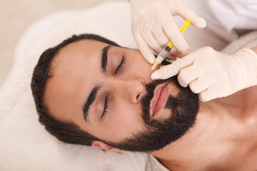 Top view close up of a bearded man getting face filler injected by cosmetologist