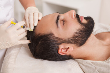 Fototapeta na wymiar Bearded man getting anti hair loss treatment by beautician