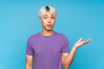 Fototapeta premium Young asian man over isolated blue background making doubts gesture