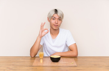 Obraz na płótnie Canvas Young asian man with matcha tea in a table showing an ok sign with fingers