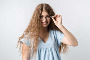 Portrait of charismatic modern girl with curly long hair in casual light clothes and wears round spectacles posing isolated on white wall background. People lifestyle concept