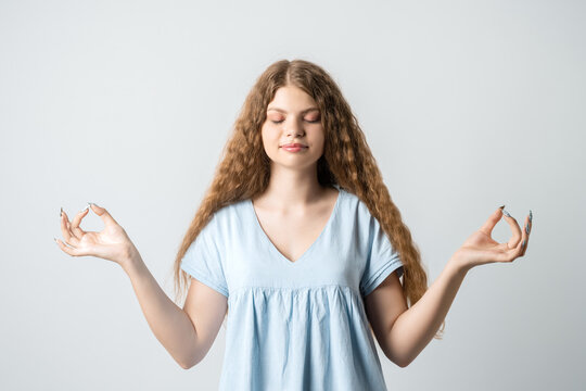Calm young woman practices yoga indoor, shows OKAY sign with both hands, demonstrates approval, isolated over white background. People, peace and meditation concept.