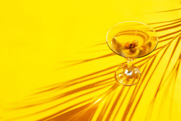 Glass of martini and the shadow of palm leaves on a yellow background. Trend contrasting shadows
