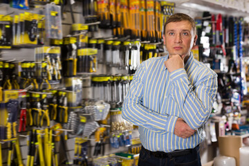 Fototapeta na wymiar Portrait of ordinary male who is standing near showcase in the tools store