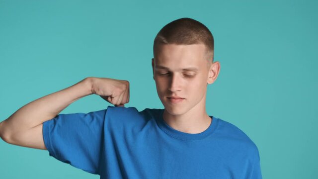 Handsome strong guy confidently showing biceps muscles on camera over colorful background. Power expression