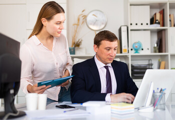 Confident businessman and young female colleague working with papers and laptop in modern office..