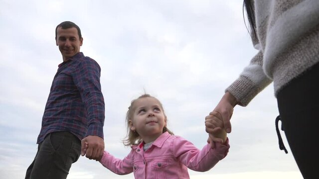 A happy family walks in the Park under the rays of the sun at sunset. Mom, dad and baby holding hands walk in the fresh air, lead a healthy lifestyle.