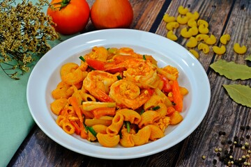 Stir fried macaroni with shrimps and tomato sauce surrounded by key ingredients on wooden table.