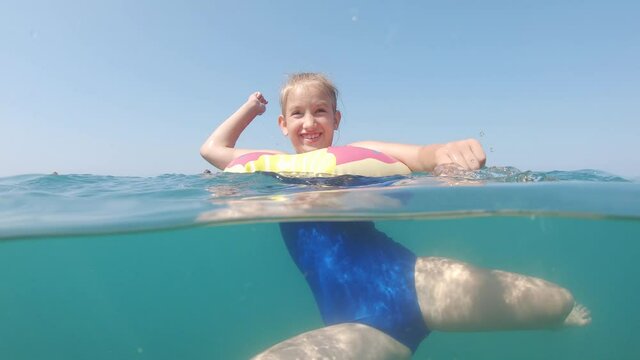 Cute child girl bathes in sea. She is learning to swim. Family vacation concept.
