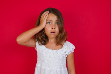 Embarrassed attractive Little caucasian girl with blue eyes wearing white dress standing over isolated red background, with shocked expression, expresses great amazement, Puzzled man poses indoor