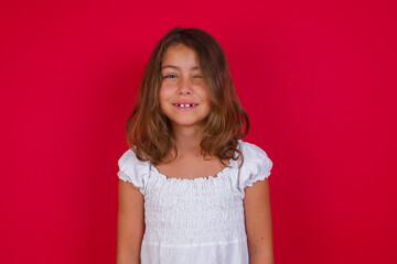 Positive coquettish Little caucasian girl with blue eyes wearing white dress  smiling happily, blinking at camera in a playful manner, flirting with you. Human facial expressions and emotions
