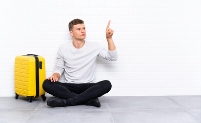 Young handsome man sitting on the floor with a suitcase touching on transparent screen