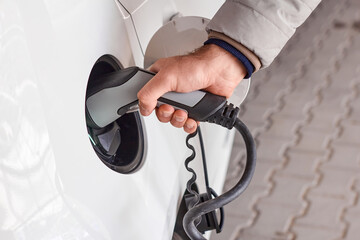 Man using a power cable and plug for charging of electric car at EV charging station. 
