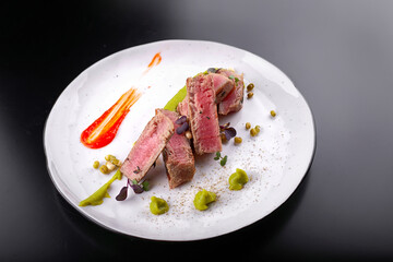 Filet mignon with capers, on a white plate, on a dark background