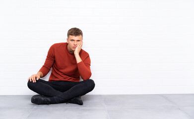 Young handsome man sitting on the floor unhappy and frustrated