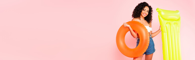 panoramic crop of cheerful african american girl holding swim ring and inflatable mattress isolated...
