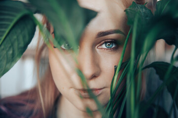 Naklejka premium face of a girl with green eyes and blond hair close-up and a branch of a plant in front of the face