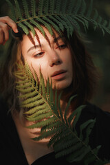 dark-haired girl with 
fern in her hands near face and sun glare on her face