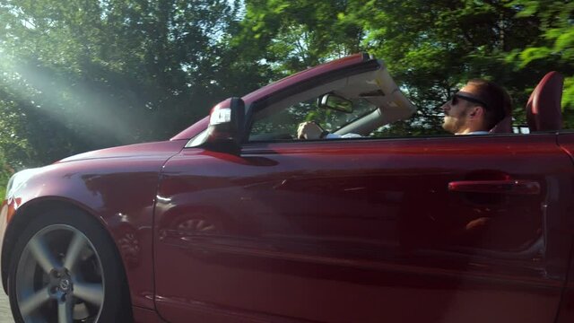 The man is riding in a convertible. Beautiful red cabriolet car driving