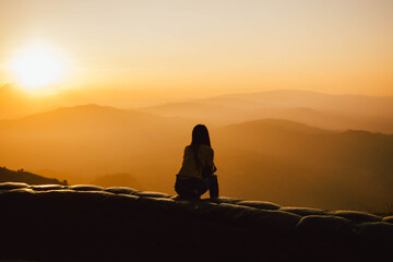 Silhouette of a girl sitting on a cliff side looking at the sunset.  Beautiful sunset background.