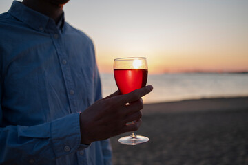 Man with glass of wine on beach at sunset