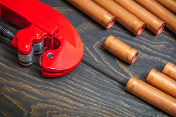 Red pipe cutter and copper pipes with connectors for plumbing repairs on black wooden boards close up