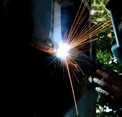 Welder welds metal on machine with sparks