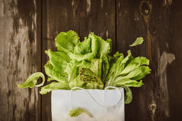 Lettuce leaveson in a paper bag a wooden dark table. Batavia salad. Authentic still life with green...