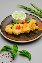 Shrimp fries in breadcrumbs on a gray background decorated with basil, sea salt and pepper. Snacks on the restaurant menu.