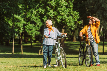 Obraz premium Smiling grey haired couple standing near bikes on meadow in park