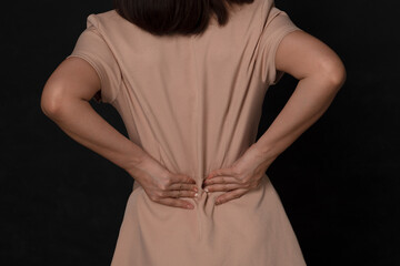 Obraz premium Backache concept bending over in pain with hands holding lower back on black background; Injured business woman with lower back spinal pain. Free from copy space.