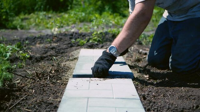 Man lays a gray paving tile.