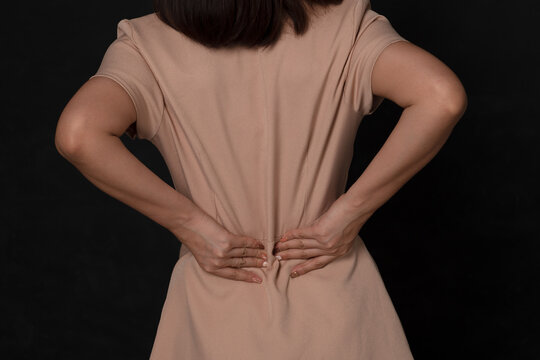 Backache Concept Bending Over In Pain With Hands Holding Lower Back On Black Background; Injured Business Woman With Lower Back Spinal Pain. Free From Copy Space.