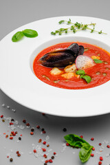 Tomato soup mashed with seafood mussels in a white plate on a gray background.