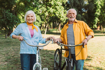 Fototapeta na wymiar Positive elderly couple smiling near bikes in summer park
