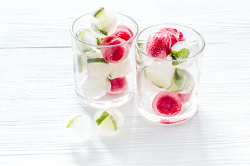 Cocktail glasses with berries in ice cubes on white table copy space