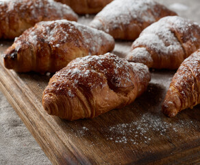 baked croissants sprinkled with powdered sugar lie on a brown wooden board