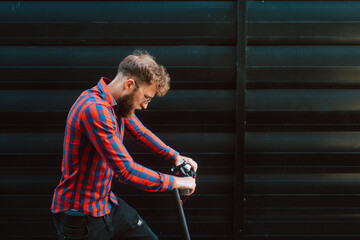 A handsome young caucasian bearded businessman rides a scooter in front of a black wall
