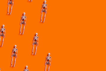 Holiday card, Halloween horror story. Halloween decoration flat lay - orange background with skeletons in pastel colors. A place for your text.