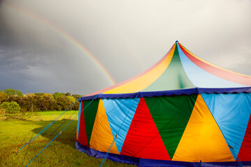 Colored circus tent in a rainy day with a rainbow on the sky