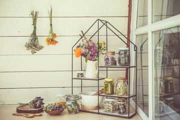 Collection of various herbal medicinal plants dry in glass jars and drying on wall. Modern shelf with jars mortar and pestle and bouquet of herbal wildflowers in ceramic jug. Retro vintage filter.