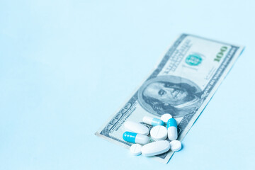 Scattered pharmaceutical tablets, medicine pills and capsules on dollar money on blue background....