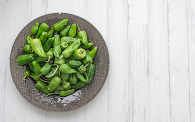 padrón peppers in a dark ceramic plate on white wooden background