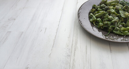 padrón peppers in a dark ceramic plate on white wooden background
