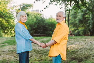 Fototapeta premium Elderly couple smiling at camera while holding hands in park
